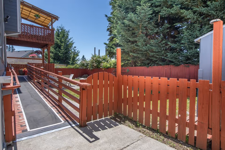 Red wooden fenced yard with a gated entrance and an accessible ramp alongside a building under a clear blue sky.