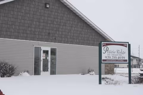Snow-covered exterior of Prairie Ridge Assisted Living with front entrance and sign.
