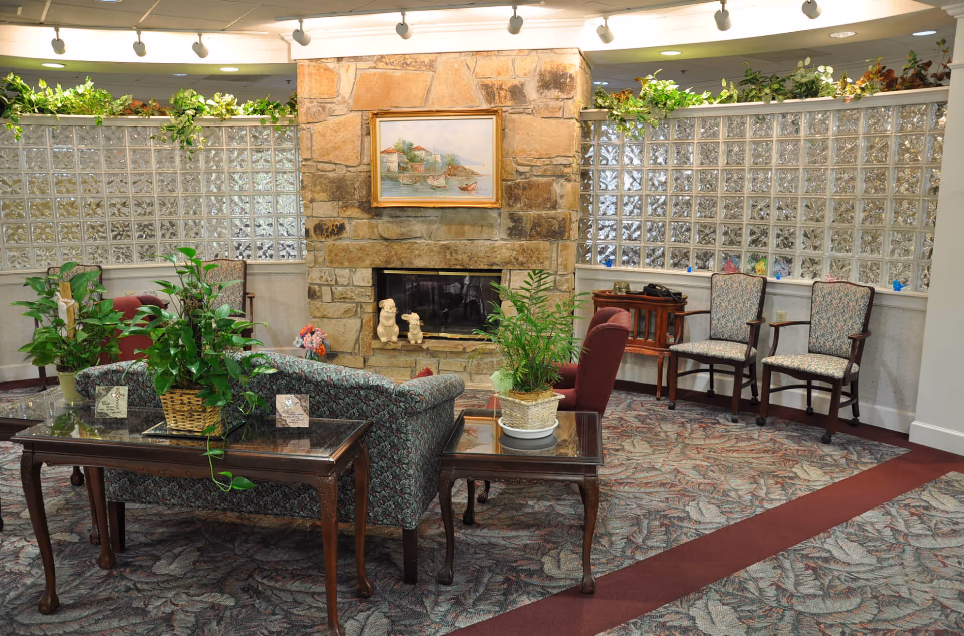 Comfortable lounge area with sofas, chairs, potted plants and a stone fireplace beneath a framed painting.