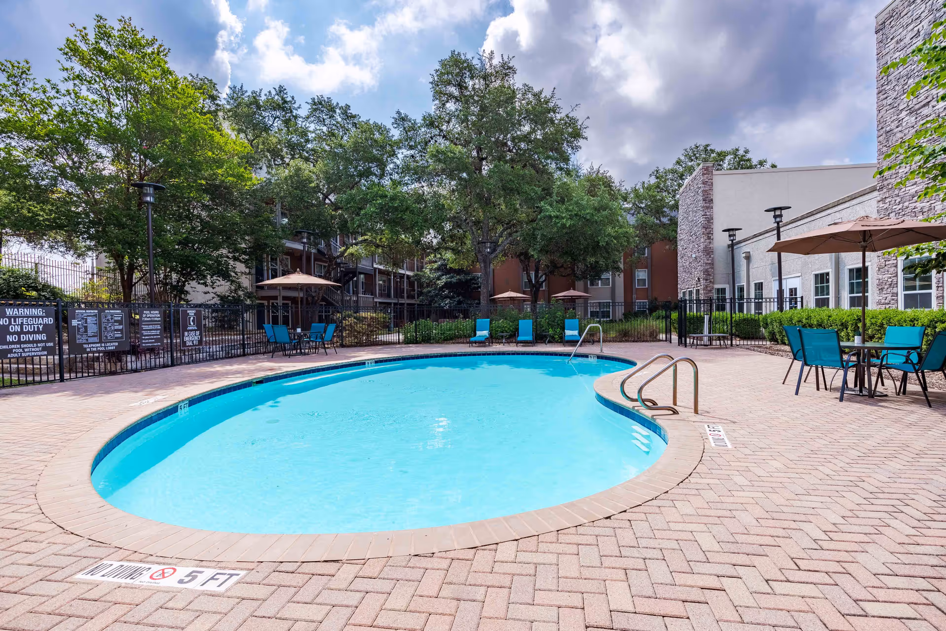 A view of the outdoor pool area at New Forest Haven, featuring a circular pool surrounded by lounge chairs and umbrellas, with trees and a building in the background.