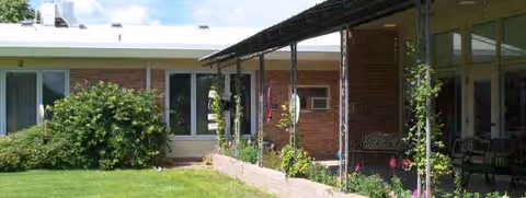 Exterior view of a single-story senior living center with a covered porch and green lawn.