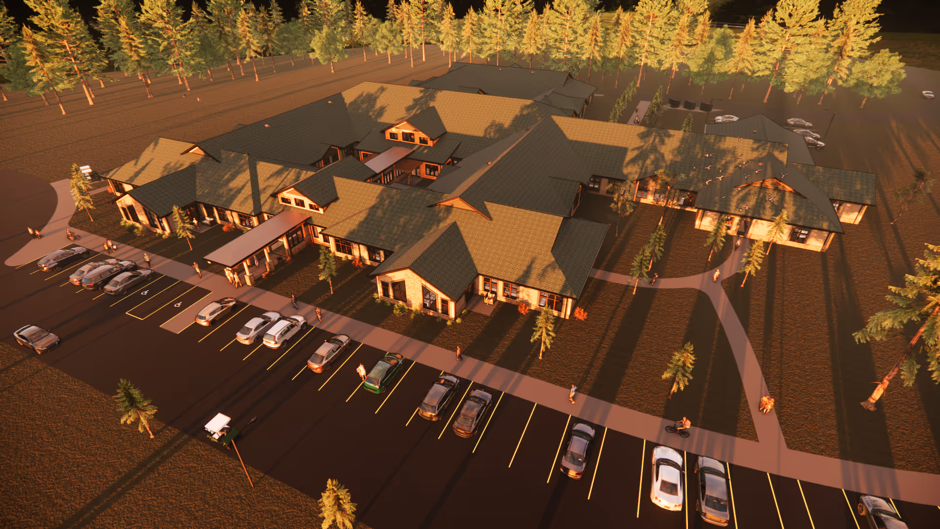 Aerial view of a senior living facility named Riverwood Senior Living a Frontida Community, showing multiple connected buildings with green roofs surrounded by trees. There is a parking lot with several cars and pathways leading through landscaped grounds.