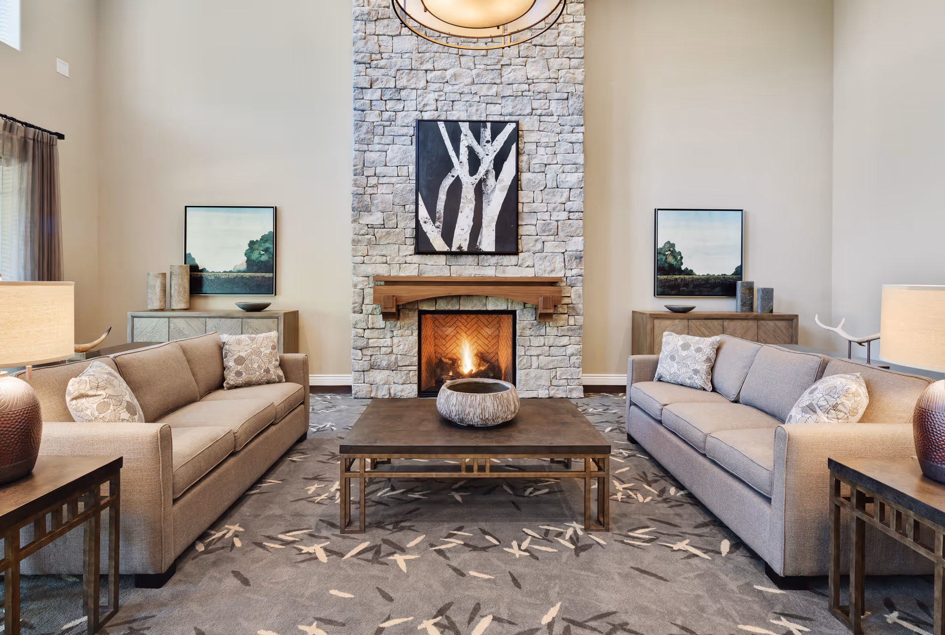 Spacious communal living room with two sofas facing a stone fireplace, coffee table, and wall art.