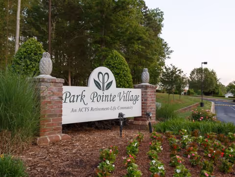 Entrance sign reading "Park Pointe Village" set between brick pillars with landscaping and trees around it.