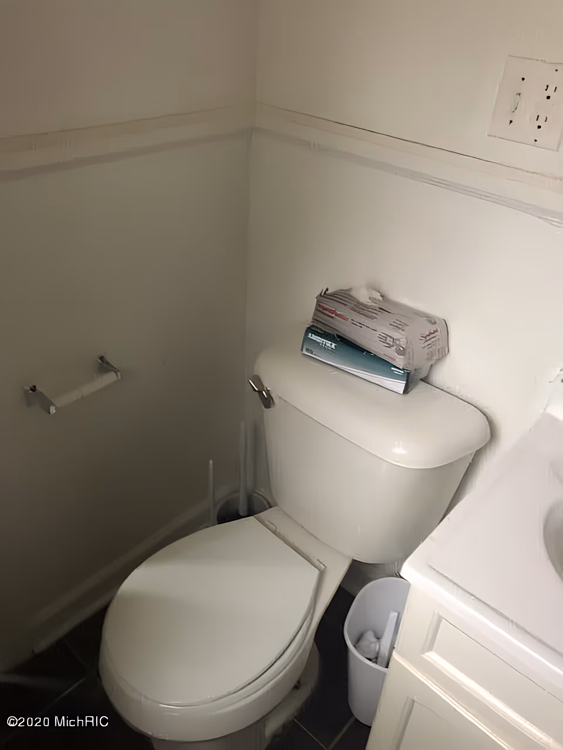Small bathroom corner showing a toilet with a tissue box on the tank, an empty toilet paper holder, and part of a sink cabinet.