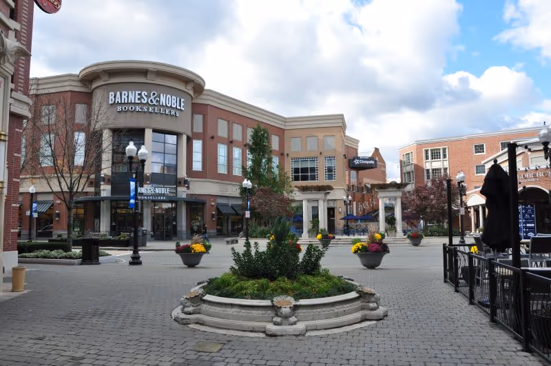 Open pedestrian plaza with a Barnes & Noble storefront, decorative planters and outdoor seating under a cloudy sky.