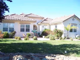 A single-story white villa-style senior living facility with a manicured lawn and landscaped entrance.