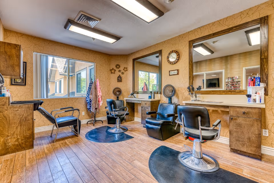 Interior salon/hair-styling room with chairs, mirrors, and a wash station in a senior living facility.