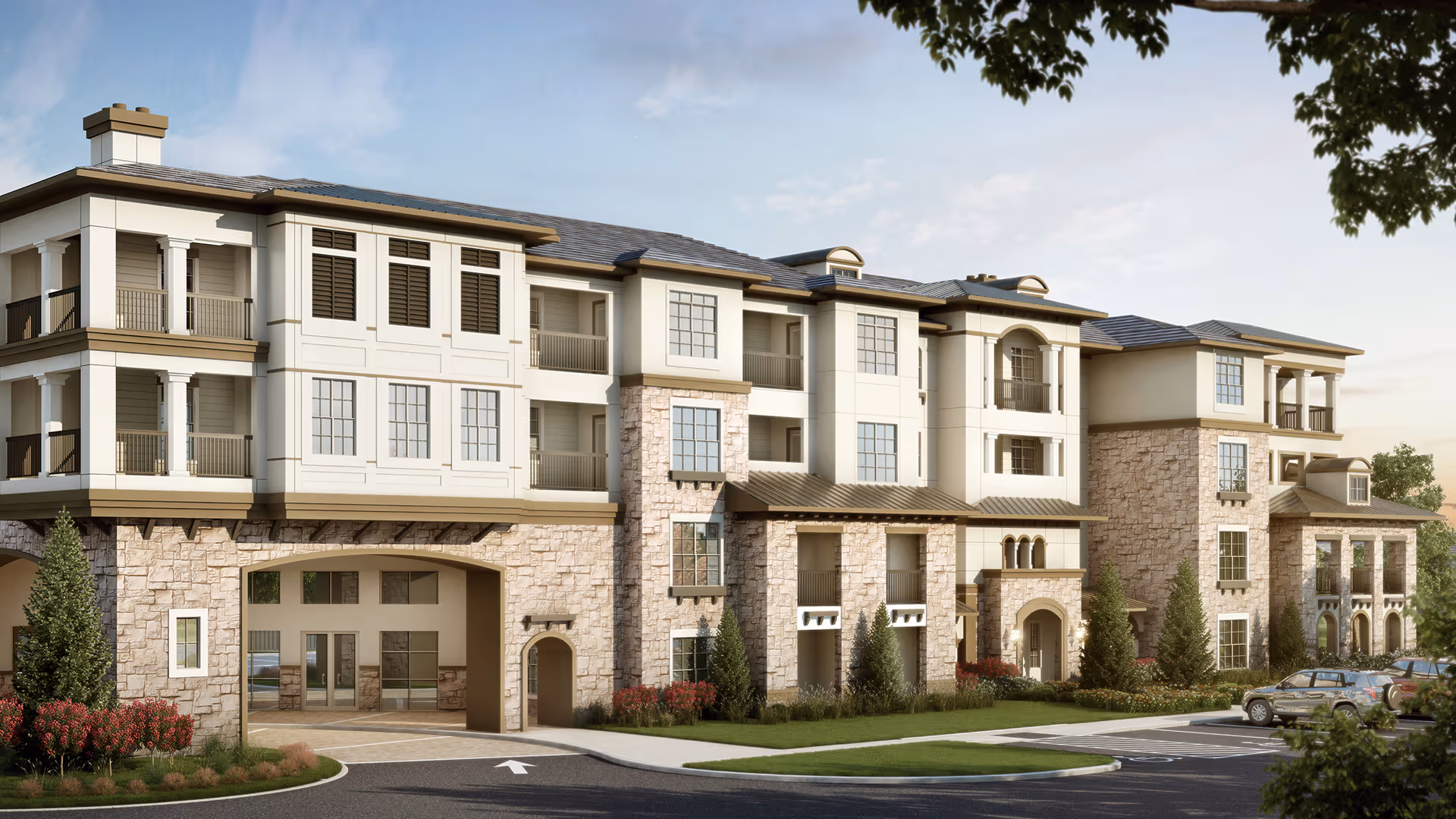Front exterior of a multi-story senior living building with stone and stucco facade, balconies, landscaping and a driveway entrance.