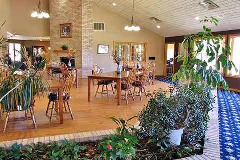 Indoor dining area with wooden tables, chairs, plants, and large windows.