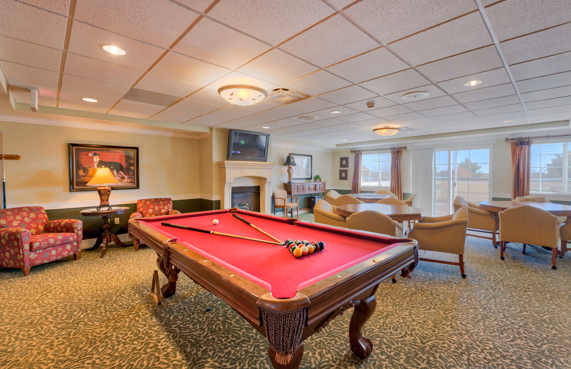 Common area interior featuring a red-felt pool table surrounded by chairs, tables, a fireplace and a wall-mounted TV.