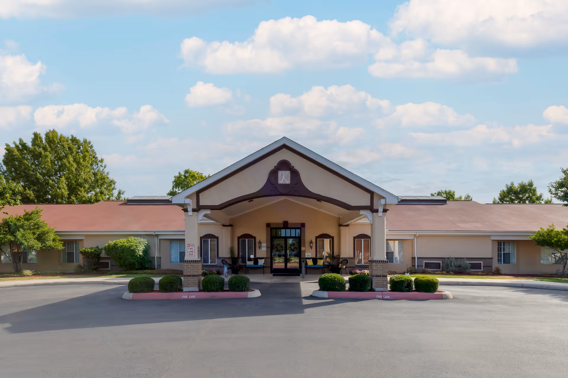 Front exterior view of Brookdale Medical Center Kingsley building with a covered entrance, surrounded by trimmed bushes and trees under a partly cloudy sky.