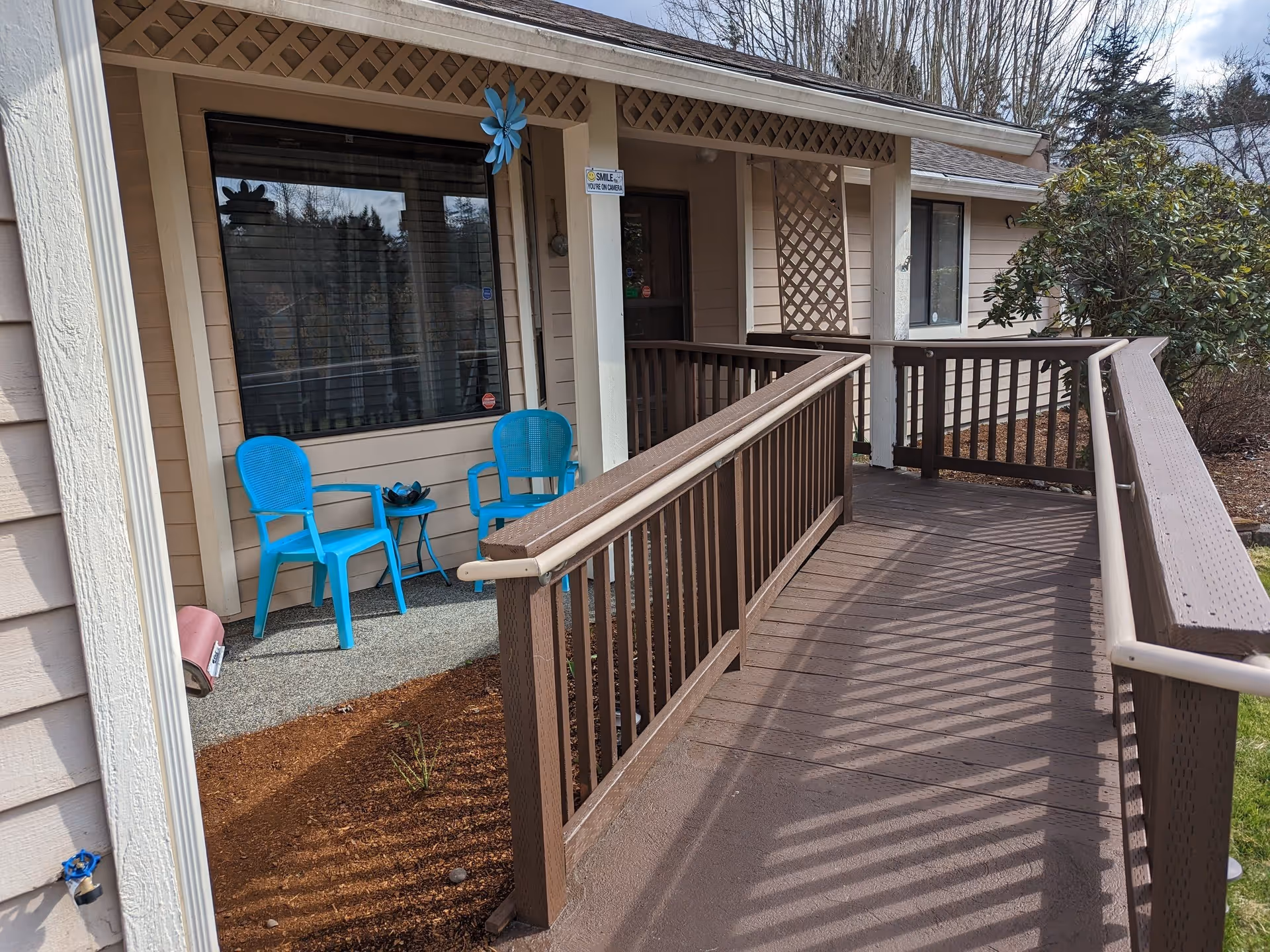 Front entrance ramp and porch of a single-story adult family home with two blue chairs and a small table.