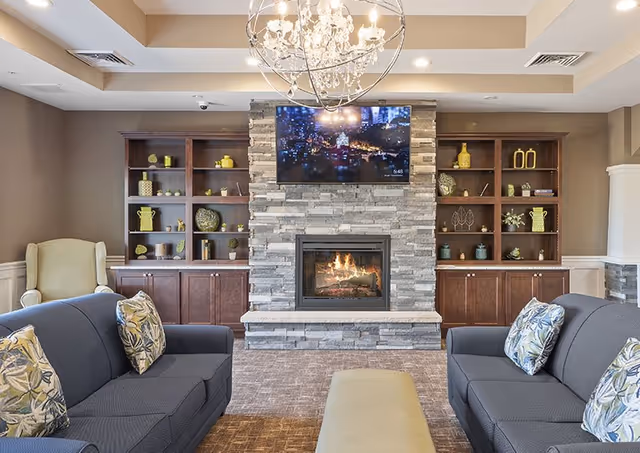 Comfortable living room with sofas facing a stone fireplace and mounted TV flanked by built-in wooden shelving.