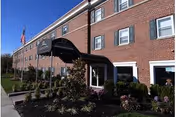 Brick facility exterior with black awning entrance, American flag, and manicured shrubs.