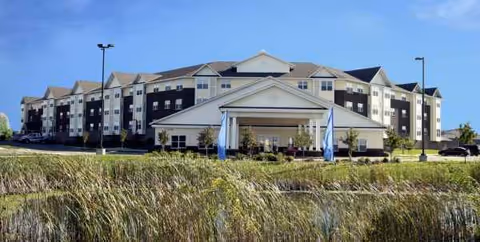 A large Heritage Place senior living building with a central entrance and surrounding lawn.