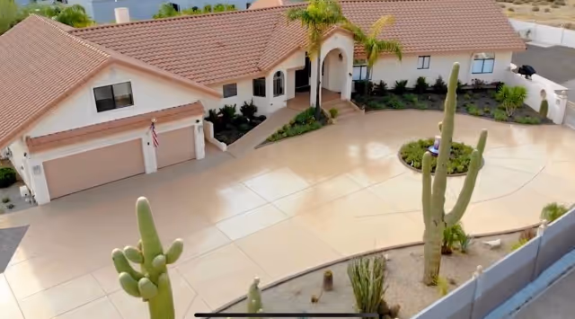 Aerial view of a single-story stucco building with a tiled roof, circular driveway and desert landscaping featuring tall cacti.
