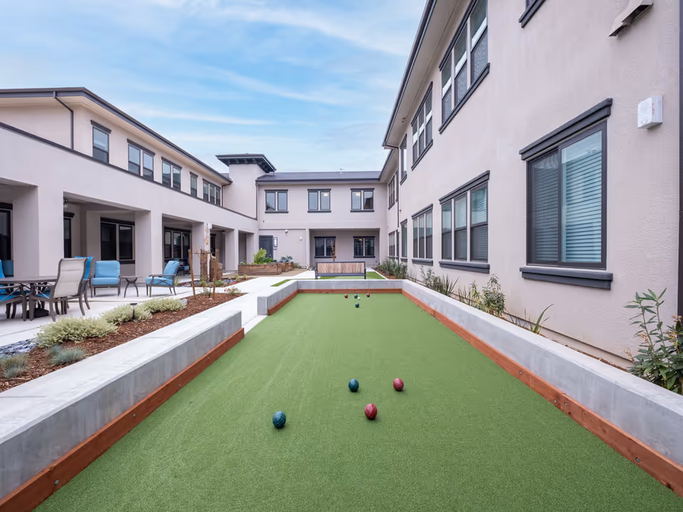 Outdoor courtyard with a bocce turf, seating area, and two-story building wings on either side.