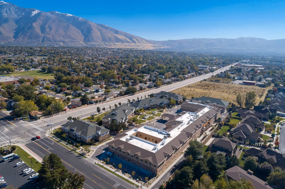 Aerial view of Mission At Crescent Senior Living facility surrounded by residential neighborhoods and roads, with mountains in the background under a clear blue sky.