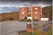 Exterior view of a three-story brick building labeled Putnam Nursing & Rehabilitation Center, with a parking area in front and hills with autumn foliage in the background under a cloudy sky.