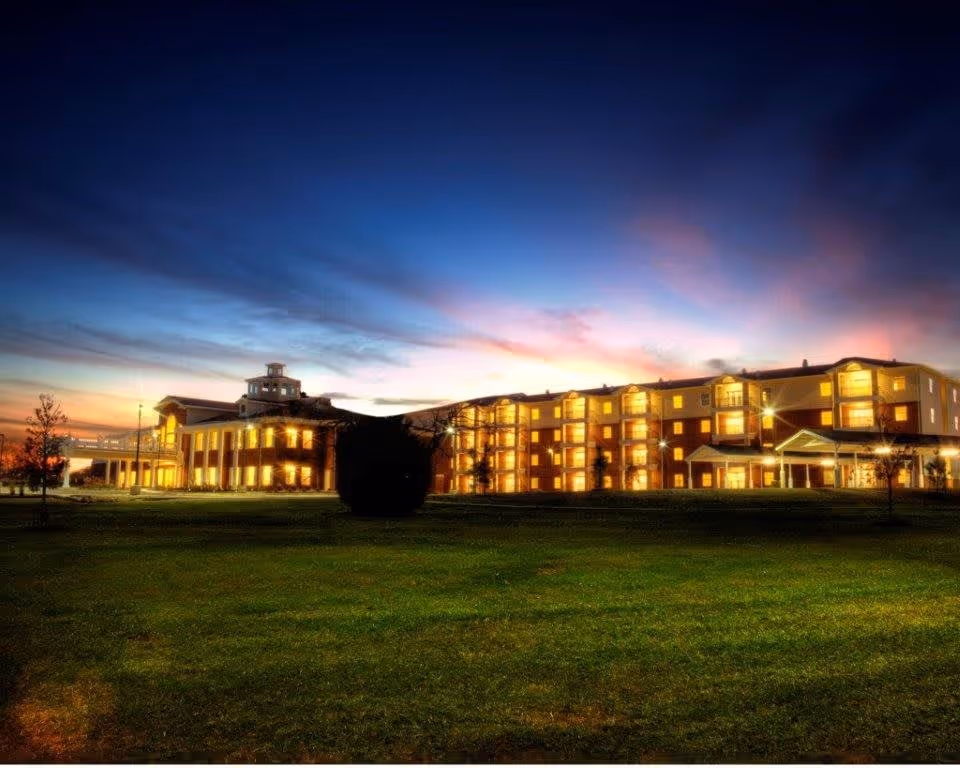 Exterior view of Meadow Lake Senior Living building at dusk with lights glowing warmly from the windows and a clear sky transitioning from sunset to night.