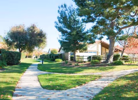 A well-kept senior living facility exterior with a walkway through green lawn.