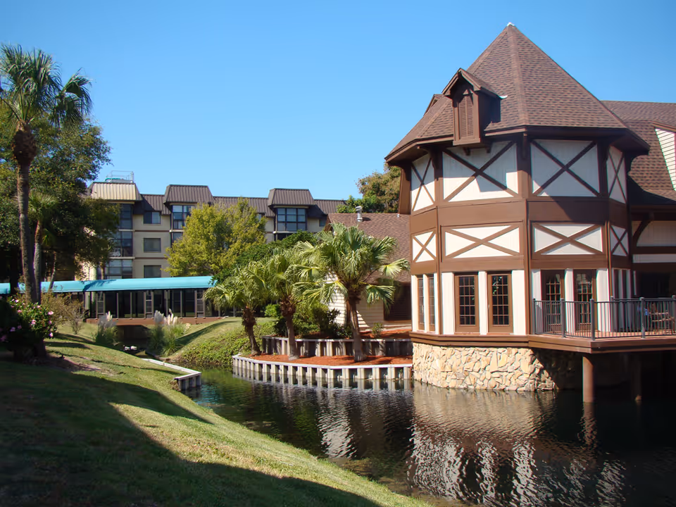 Timber-framed building beside a waterway with palm trees and landscaping.