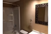 Small bathroom with a bathtub/shower combo, toilet, sink vanity and a decorative wall mirror.