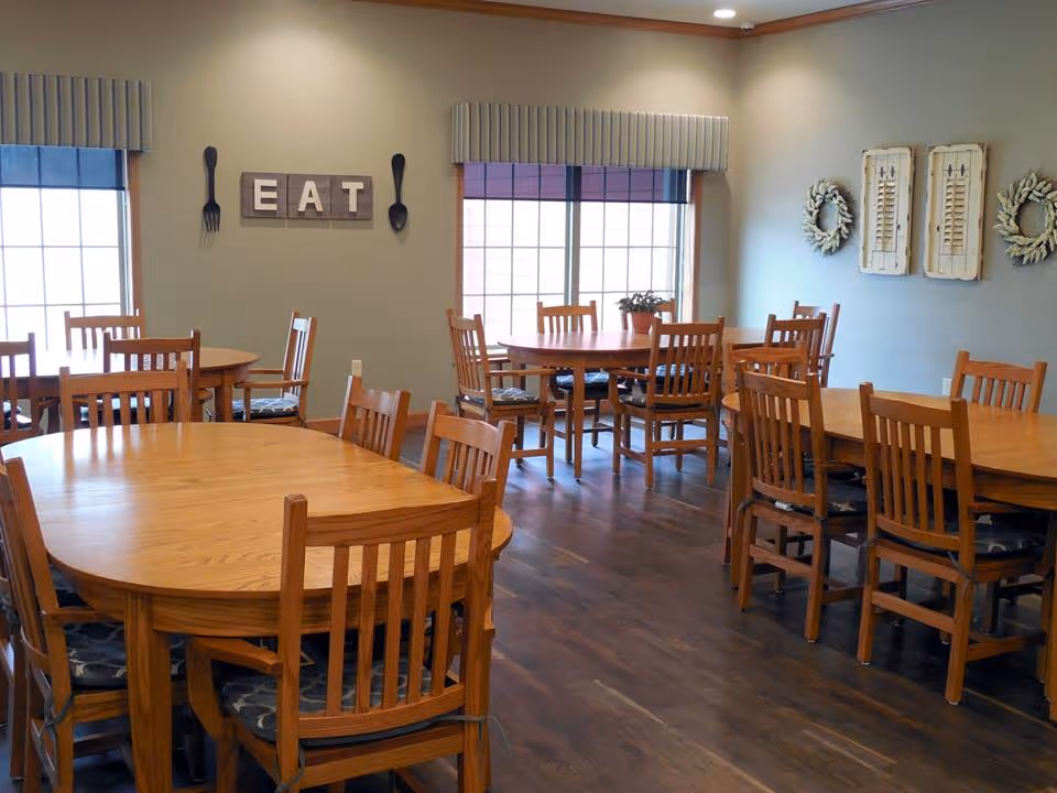 Dining room with multiple wooden tables and chairs, windows, and wall decor spelling "EAT".