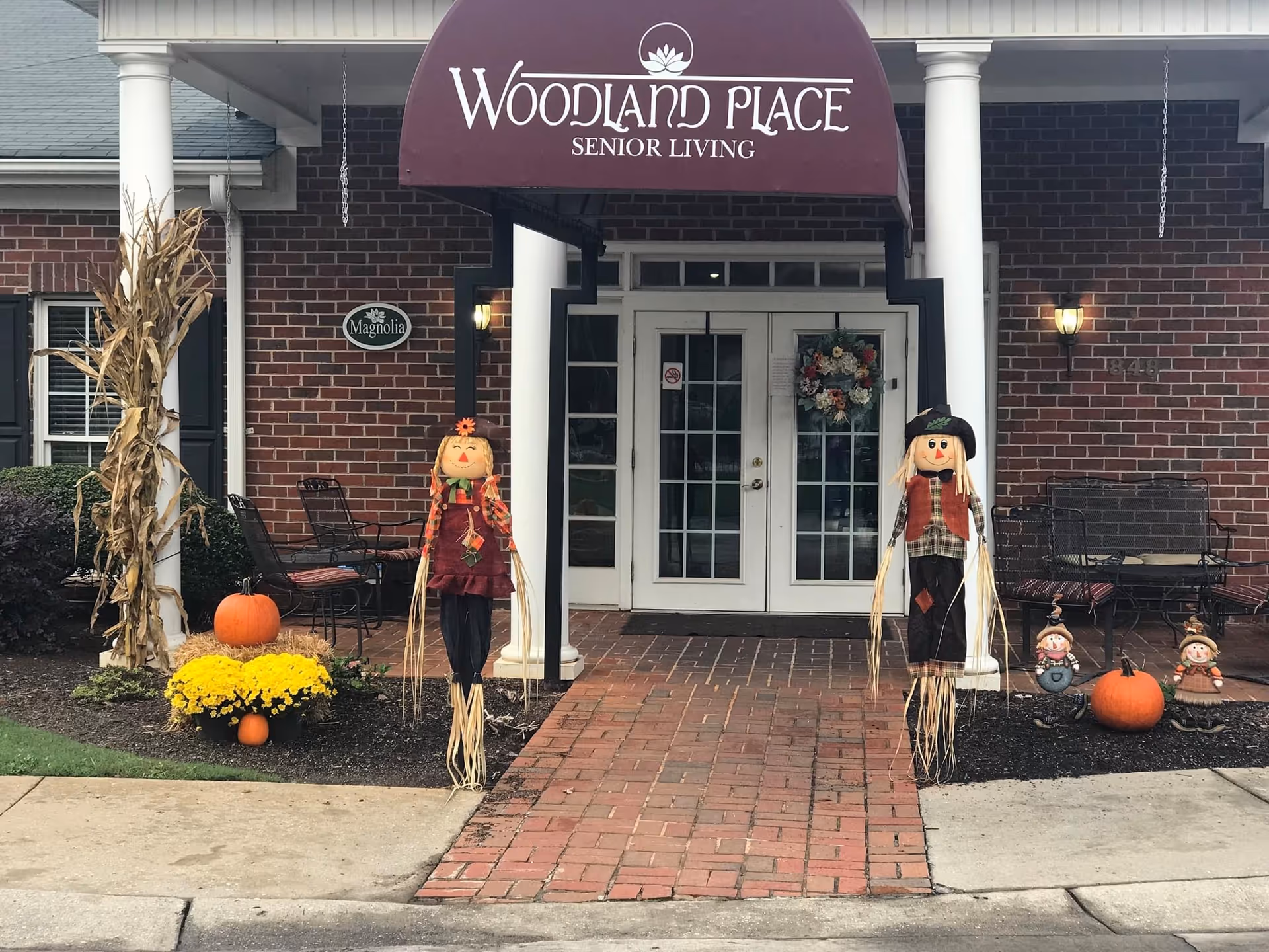 Front entrance of Woodland Place Senior Living adorned with pumpkins and scarecrows.