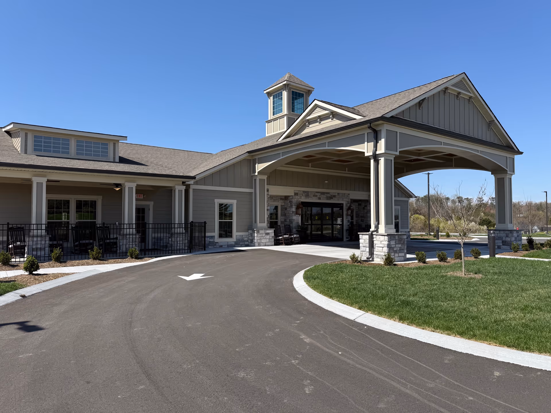 Exterior view of The Lantern at Morning Pointe Alzheimer's Center of Excellence, Hardin Valley - Phase II building entrance with a covered driveway, stone pillars, and a clear blue sky.