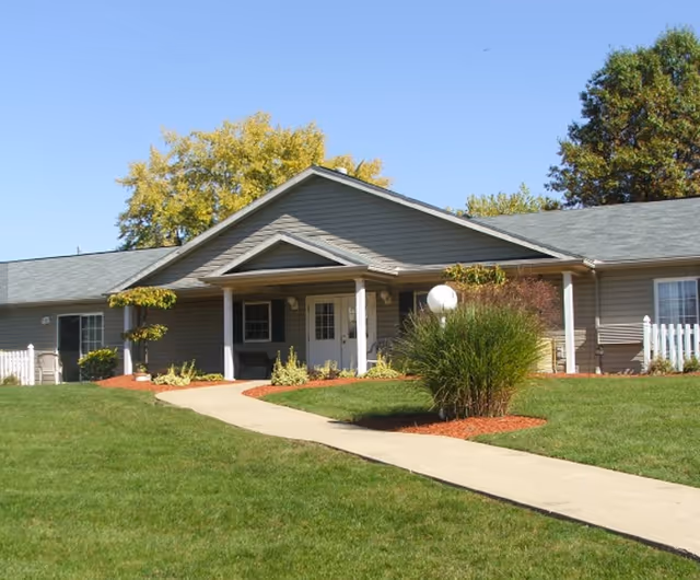 Single-story senior living building with a covered entrance, walkway, and landscaped lawn.