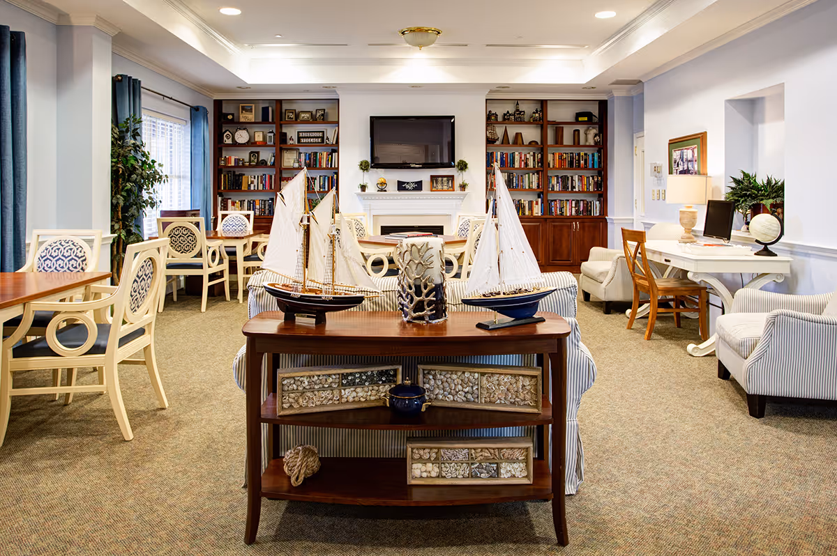 Bright communal living room with sofas, tables, bookshelves and decorative model sailboats on a console table.