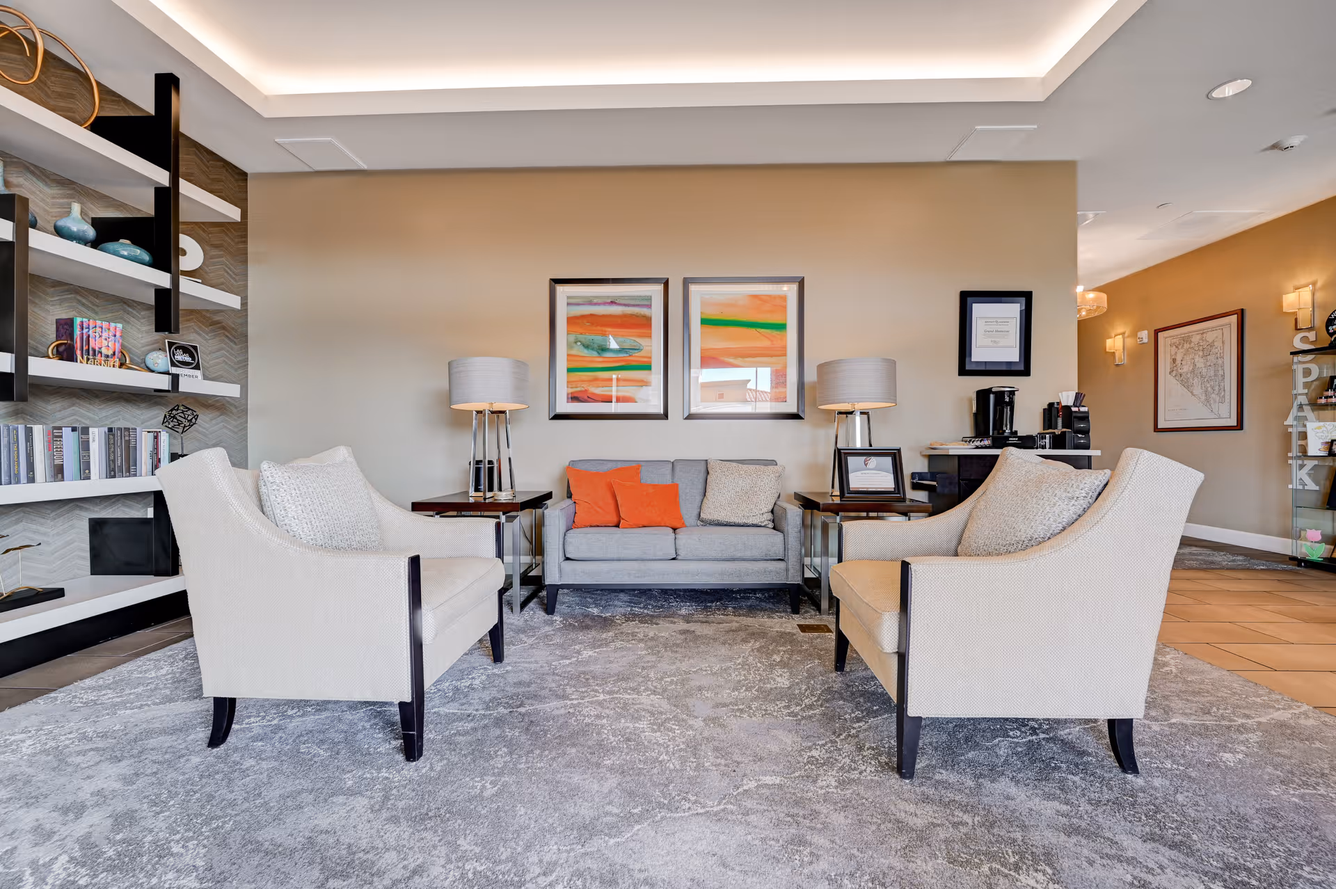 Cozy communal seating area with a sofa, two armchairs, side tables, lamps, artwork, and built-in bookshelves.