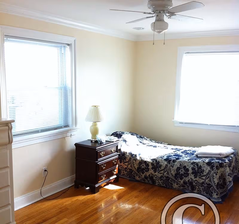 A small bedroom in Assisted Living of Potomac with a single bed and two windows.