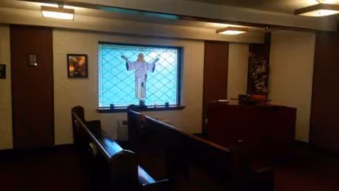 Interior chapel area with wooden pews facing a stained-glass window in a senior living facility.