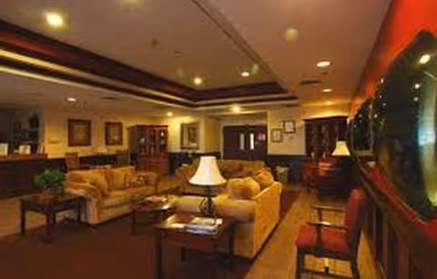 Interior lounge area with beige sofas, coffee tables, lamps, and framed art.