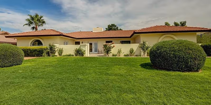 Single-story beige assisted living building with a red tile roof, arched windows, and a manicured lawn