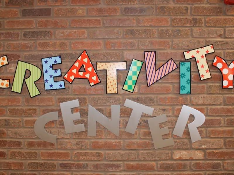 A brick wall with colorful, patterned letters spelling out 'CREATIVITY' and plain silver letters below spelling 'CENTER'.