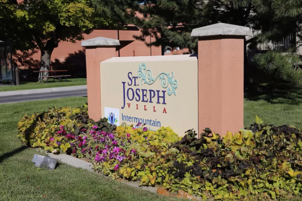 Entrance sign reading 'St. Joseph Villa' surrounded by landscaped flowers and greenery in front of the building.