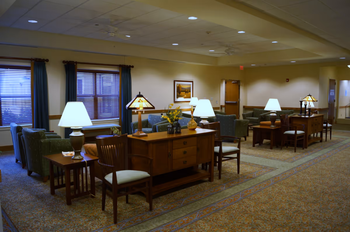 Spacious furnished common lounge with sofas, armchairs, wooden tables and lamps in a senior living facility.