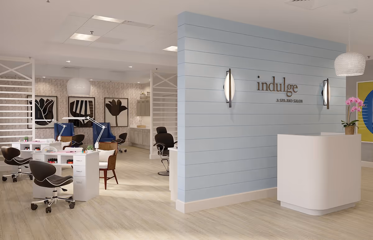 Interior view of a spa and salon area named 'indulge' at Watersound Fountains, featuring manicure stations with chairs and nail polish, a reception desk with a pink orchid, modern wall lights, and framed floral artwork on the walls.