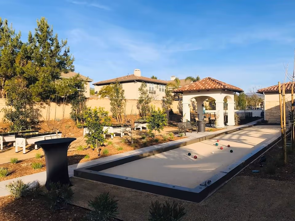 Outdoor courtyard with a bocce ball court, gazebo, benches, and landscaping under a clear blue sky.