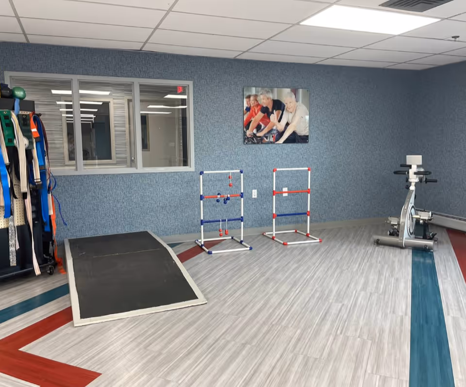 A senior facility exercise/therapy room with a stationary bike, ramp, mobility equipment and a wall photo of seniors cycling.