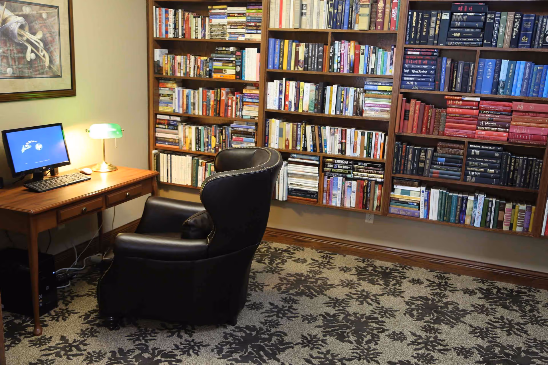 Cozy reading room with bookshelves, a leather armchair, and a desk with a computer and lamp.
