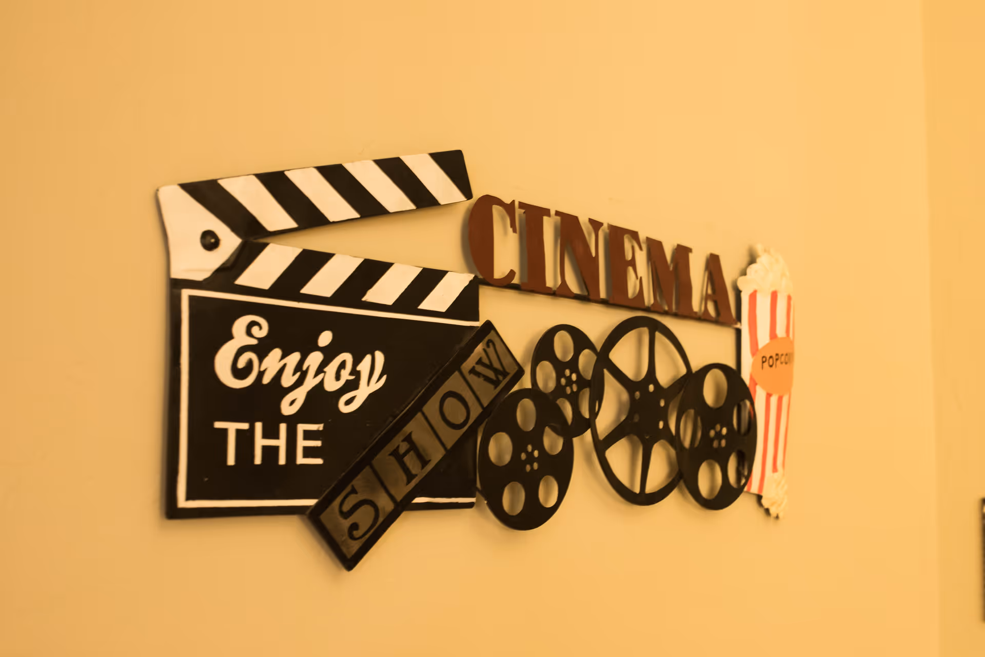 Wall decoration featuring a movie clapperboard with the words 'Enjoy the Show', film reels, the word 'CINEMA' in large letters, and a popcorn container illustration.