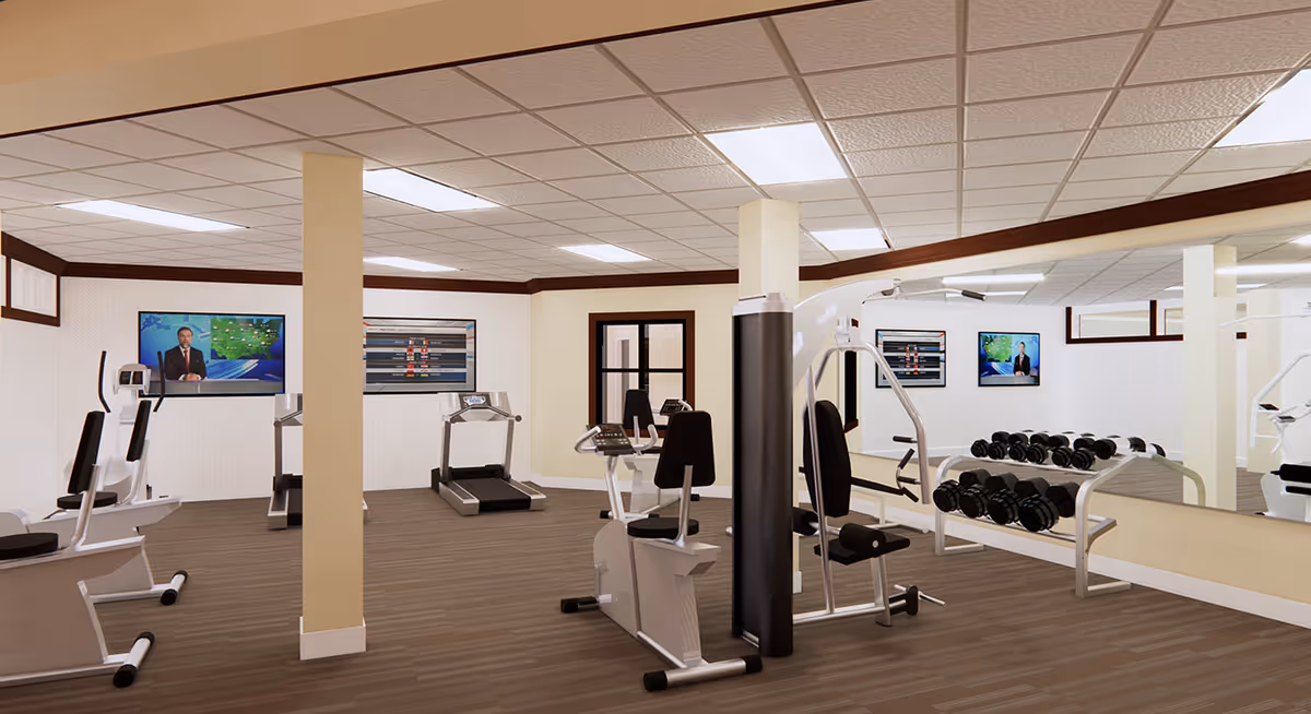 A fitness room with exercise equipment including stationary bikes, treadmills, weight machines, and a rack of dumbbells. The room has a large mirror on one wall and two televisions mounted on the opposite wall. The floor is wood-patterned, and the ceiling has recessed lighting.