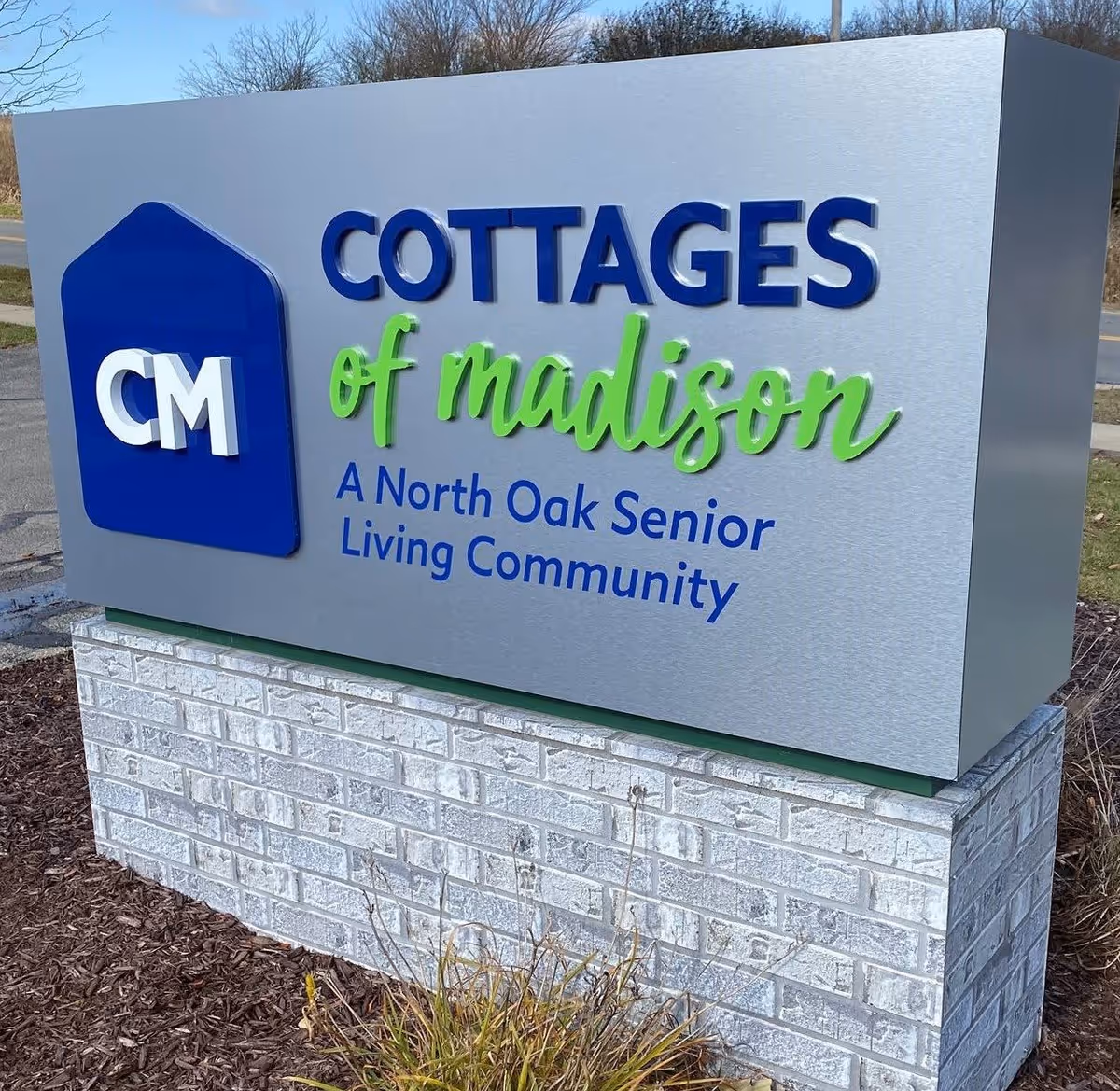 Monument sign at the entrance reading "Cottages of Madison — A North Oak Senior Living Community."