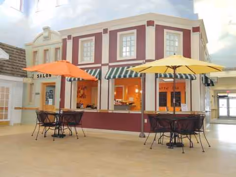 Indoor recreation area featuring a storefront-style cafe with striped awnings and outdoor-style seating.