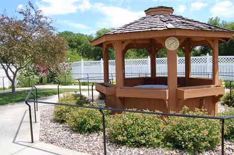 Wooden gazebo in a landscaped outdoor courtyard with a white fence.